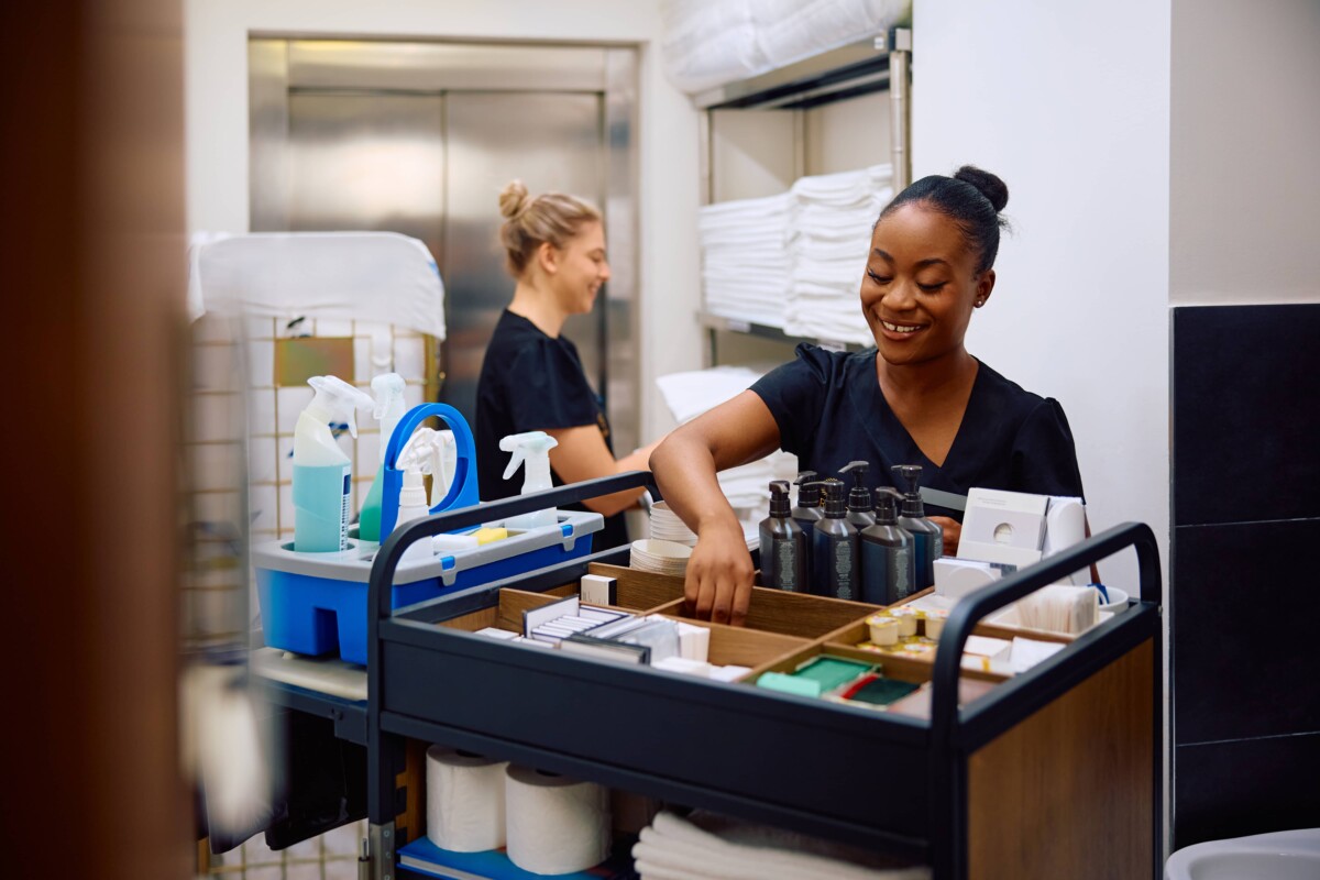 Happy black chambermaid restocking housekeeping trolley while working in a hotel.