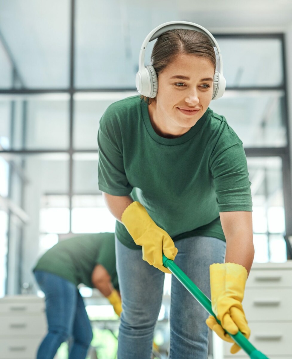 Shot of a young woman cleaning an office with her colleague in the background.jpg
