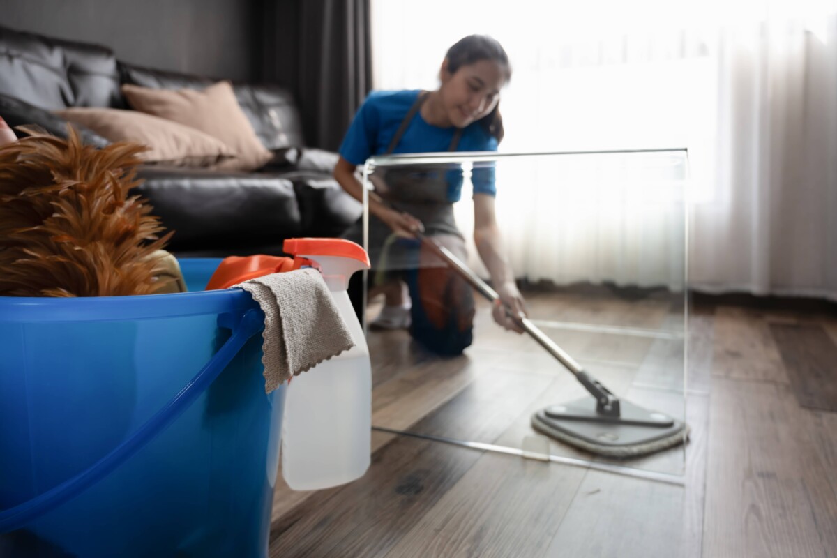 Young woman in an apron wiping laminate flooring in the living room with microfiber wet mop